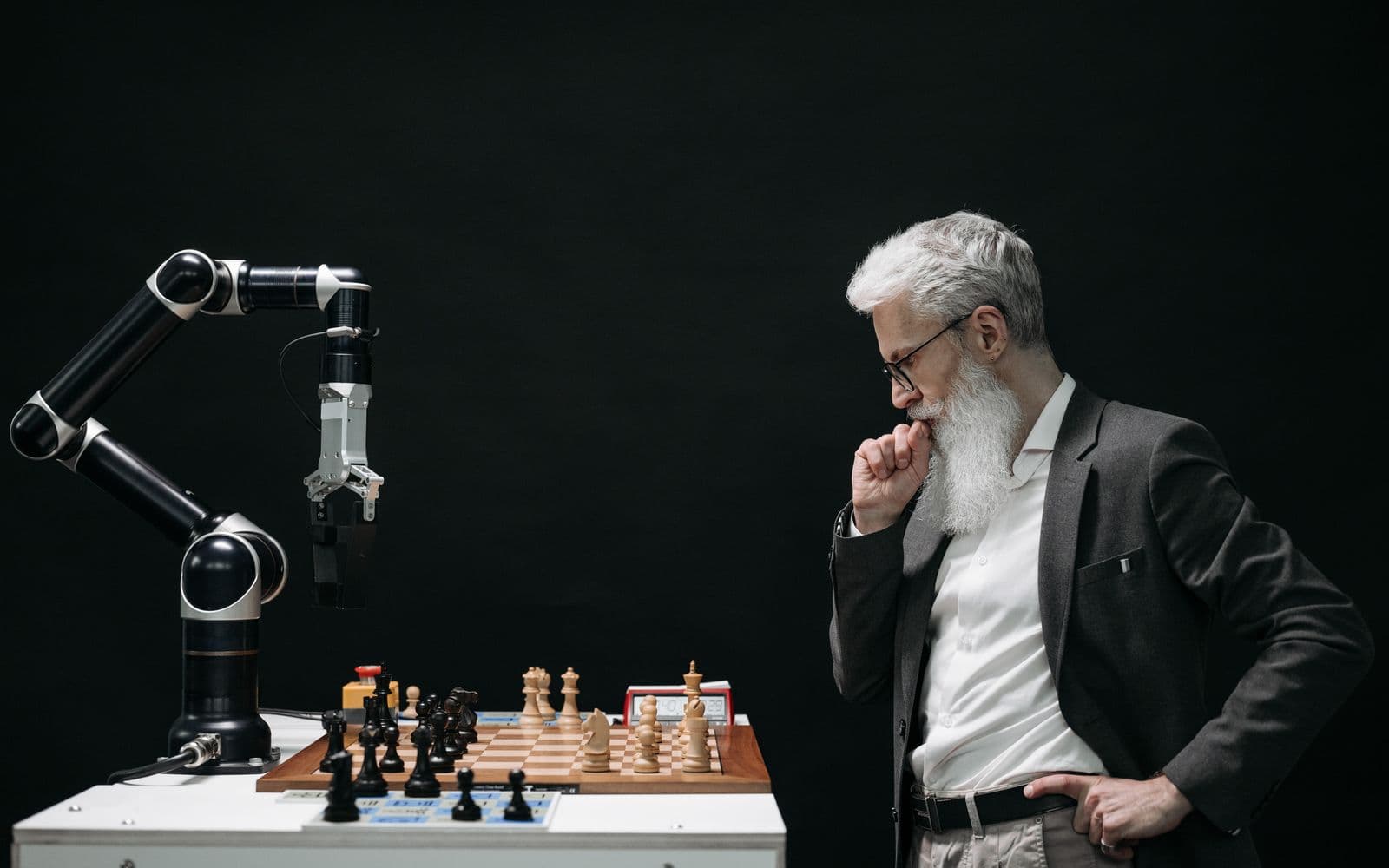 A person considering a chessboard opposite a robotic arm.